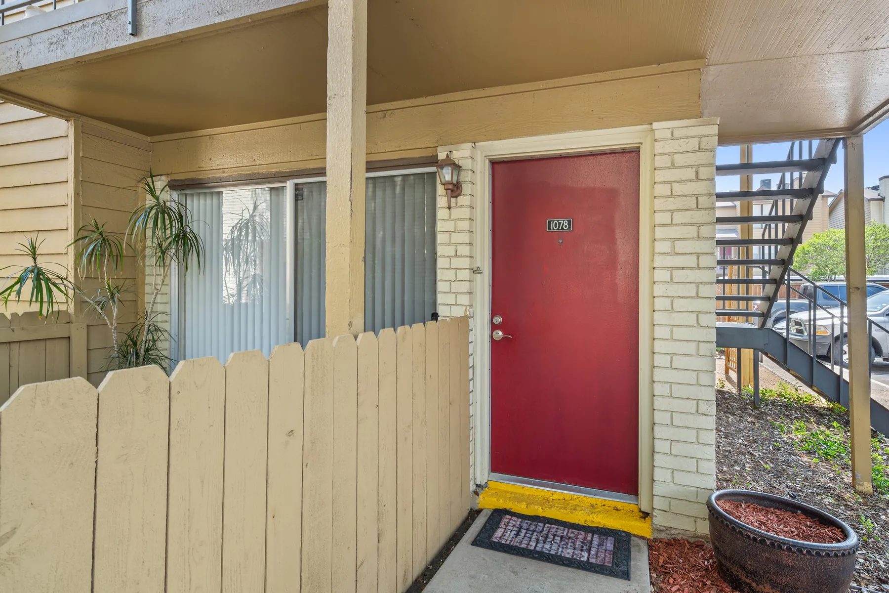 Ground-floor apartment entry with a red front door and a fenced patio at Regal Court